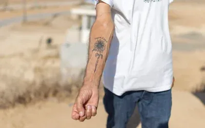 Danny, un habitant du kibboutz Nahal Oz, montrant le tatouage à l'encre noire représentant un tournesol qu'il porte sur l'avant-bras, accompagné d'une inscription en hébreu signifiant « Le chemin vers l'espoir », qu'il s'est fait faire en mémoire du pogrom perpétré par le groupe terroriste palestinien du Hamas le 7 octobre 2023, à Nahal Oz, dans le sud d'Israël, le 22 octobre 2026. (Crédit : Ilia Yefimovich/AFP)