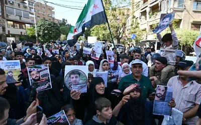 Des Syriens agitent des drapeaux et brandissent des portraits de personnes qui auraient été arrêtées lors d’incursions militaires israéliennes dans le sud de la Syrie, alors qu’ils manifestent près du bâtiment des Nations unies à Damas, le 23 octobre 2026. (Crédit : LOUAI BESHARA/AFP)
