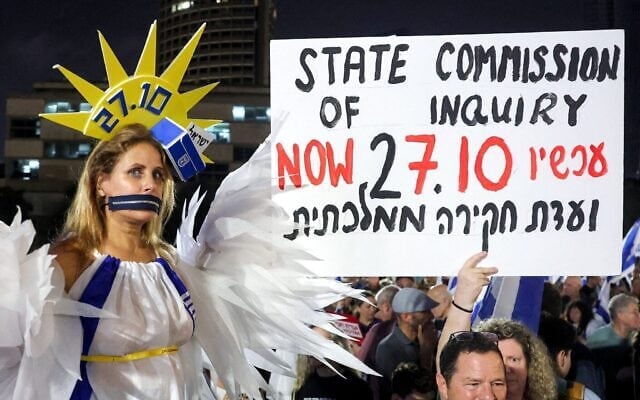 Une manifestante, la bouche recouverte d’une fermeture éclair et vêtue d’un costume, enveloppée dans le drapeau d'Israël, prenant la pose lors d’une manifestation anti-gouvernement, sur la Place des Otages, à Tel Aviv, le 24 octobre 2026, quelques jours avant les élections législatives. (Crédit : Jack Guez/AFP) Une manifestante, la bouche recouverte d’une fermeture éclair et vêtue d’un costume, enveloppée dans le drapeau d'Israël, prenant la pose lors d’une manifestation anti-gouvernement, sur la Place des Otages, à Tel Aviv, le 24 octobre 2026, quelques jours avant les élections législatives. (Crédit : Jack Guez/AFP)