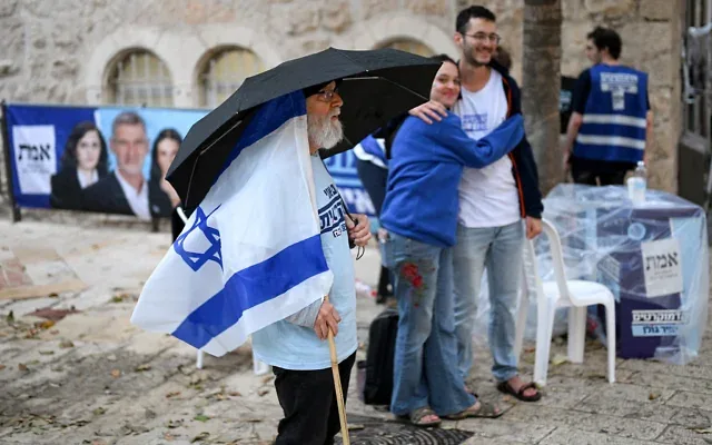 Un bénévole se tient sous un parapluie sous la pluie devant un bureau de vote à Jérusalem, le 27 octobre 2026, jour des élections législatives israéliennes. (Crédit: Jewel SAMAD/AFP) Un bénévole se tient sous un parapluie sous la pluie devant un bureau de vote à Jérusalem, le 27 octobre 2026, jour des élections législatives israéliennes. (Crédit: Jewel SAMAD/AFP)