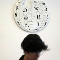 Un contributeur bénévole de Wikipédia sous le logo de Wikipédia, dans les locaux de la Fondation Wikimedia, à San Francisco, en Californie, le 12 janvier 2026. (Crédit : AP Photo/Jeff Chiu)