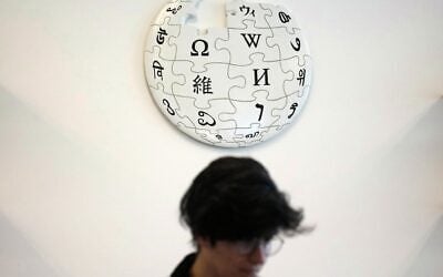 Un contributeur bénévole de Wikipédia sous le logo de Wikipédia, dans les locaux de la Fondation Wikimedia, à San Francisco, en Californie, le 12 janvier 2026. (Crédit : AP Photo/Jeff Chiu)
