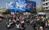 Des motards passent devant un panneau publicitaire représentant un héros légendaire persan et une silhouette volante frappant des porte-avions américains, accompagné d’un message en anglais et en farsi : "Une nouvelle puissance s’élève du golfe Persique", "L’armée de Satan sera noyée dans le golfe Persique", lors d’un défilé de motards organisé par l’État et baptisé "Janfada", ce qui signifie "Sacrifice pour l’Iran", à Téhéran, en Iran, le 25 septembre 2026. (Crédit: AP/Vahid Salemi)