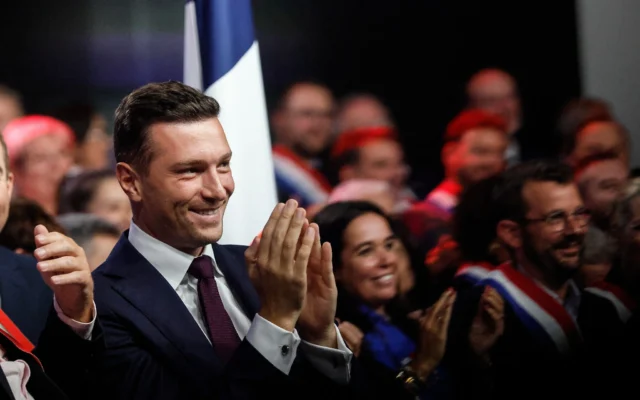 Jordan Bardella, homme politique d'extrême droite français, applaudit tandis que Marine Le Pen (hors-cadre), présidente du Rassemblement national, prend la parole à Hénin-Beaumont, dans le nord de la France, le 13 septembre 2026. (Crédit : AP/Jean-François Badias)