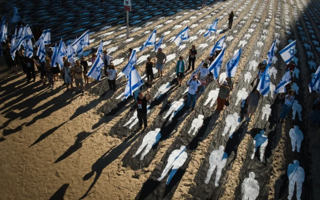 Des personnes portant des drapeaux d'Israël défilant devant une installation commémorant le troisième anniversaire du pogrom perpétré par le groupe terroriste palestinien du Hamas le 7 octobre 2023, sur le front de mer de Tel Aviv, le 7 octobre 2026. (Crédit : Oded Balilty/AP)