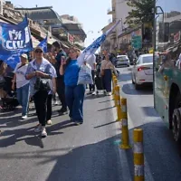 Des partisans du Premier ministre Benjamin Netanyahu défilent en brandissant des drapeaux du Likud, à côté d’un bus arborant une affiche électorale à l’effigie de son principal rival, Gadi Eisenkot, au marché Mahane Yehuda de Jérusalem, le 9 octobre 2026. (Crédit : Ohad Zwigenberg/AP)