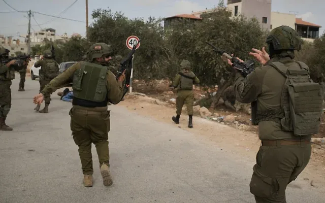 Des soldats israéliens s’approchent d’un Palestinien blessé gisant sur la route après avoir ouvert en feu en sa direction à la suite d’une attaque présumée d'extrémistes juifs contre des Palestiniens qui récoltaient des olives dans le village d’Abu Falah, en Cisjordanie, le 16 octobre 2026. (Crédit: AP/Leo Correa) Des soldats israéliens s’approchent d’un Palestinien blessé gisant sur la route après avoir ouvert en feu en sa direction à la suite d’une attaque présumée d'extrémistes juifs contre des Palestiniens qui récoltaient des olives dans le village d’Abu Falah, en Cisjordanie, le 16 octobre 2026. (Crédit: AP/Leo Correa)