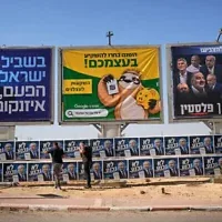 Des militants du Likud accrochant des affiches de campagne du Premier ministre Benjamin Netanyahu à côté d’un panneau publicitaire représentant son rival de l’opposition, Gadi Eisenkot, à l’approche des élections législatives israéliennes à Dimona, dans le sud d’Israël, le 21 octobre 2026. (Crédit : Ohad Zwigenberg/AP Photo)
