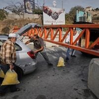 Des Palestiniens transportant des sacs de semoule devant un poste de contrôle militaire fermé à la circulation automobile, lors d'une opération de l'armée israélienne à Hébron, en Cisjordanie, le 24 octobre 2026, au lendemain de la mort de deux soldats tués par des terroristes armés dans la région. (Crédit : Mahmoud Illean/AP Photo)