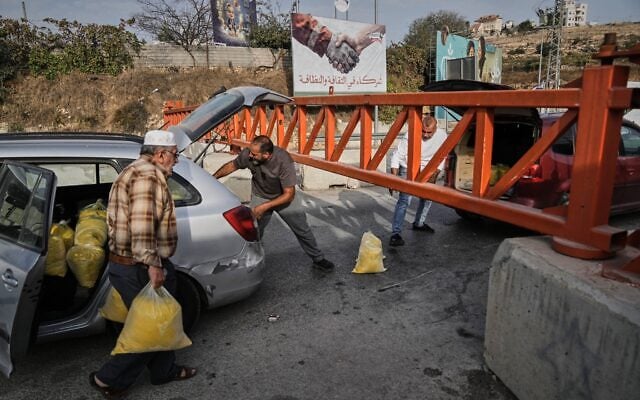 Des Palestiniens transportant des sacs de semoule devant un poste de contrôle militaire fermé à la circulation automobile, lors d'une opération de l'armée israélienne à Hébron, en Cisjordanie, le 24 octobre 2026, au lendemain de la mort de deux soldats tués par des terroristes armés dans la région. (Crédit : Mahmoud Illean/AP Photo)