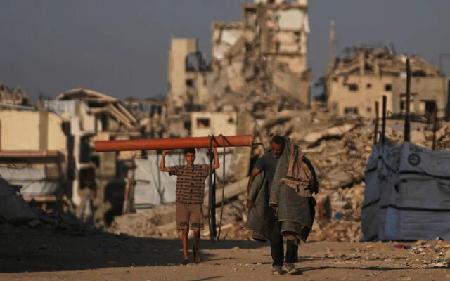 Des Gazaouis passant devant des bâtiments détruits pendant la guerre entre Israël et le Hamas, à Gaza-City, le 28 octobre 2026. (Crédit : Jehad Alshrafi/AP Photo) Des Gazaouis passant devant des bâtiments détruits pendant la guerre entre Israël et le Hamas, à Gaza-City, le 28 octobre 2026. (Crédit : Jehad Alshrafi/AP Photo)