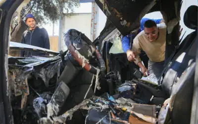 Des Palestiniens inspectant les dégâts après que des résidents d'implantation extrémistes auraient incendié quatre véhicules et tagué des graffitis en hébreu sur les murs des maisons du village palestinien d'Aqraba, au sud de Naplouse en Cisjordanie, le 6 octobre 2026. (Crédit : Nasser Ishtayeh/Flash90)