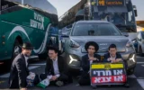 Des Haredim bloquant la circulation lors d'une manifestation contre l'enrôlement à Jérusalem, le 8 octobre 2026. Les deux manifestants à droite tiennent une pancarte sur laquelle on peut lire : « Haredi ou armée ». (Crédit : Chaïm Goldberg/Flash90)