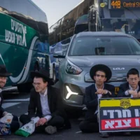 Des Haredim bloquant la circulation lors d'une manifestation contre l'enrôlement à Jérusalem, le 8 octobre 2026. Les deux manifestants à droite tiennent une pancarte sur laquelle on peut lire : « Haredi ou armée ». (Crédit : Chaïm Goldberg/Flash90)