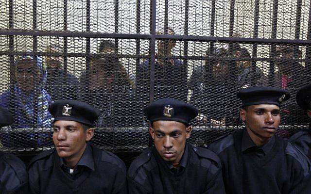 Egyptian policemen sit in front of Egyptian employees of several pro-democracy groups charged with using foreign funds to foment unrest during their trial in Cairo, Egypt. (photo credit: AP/Khalil Hamra) Egyptian policemen sit in front of Egyptian employees of several pro-democracy groups charged with using foreign funds to foment unrest during their trial in Cairo, Egypt. (photo credit: AP/Khalil Hamra)