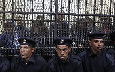 Egyptian policemen sit in front of Egyptian employees of several pro-democracy groups charged with using foreign funds to foment unrest during their trial in Cairo. (photo credit: AP/Khalil Hamra)