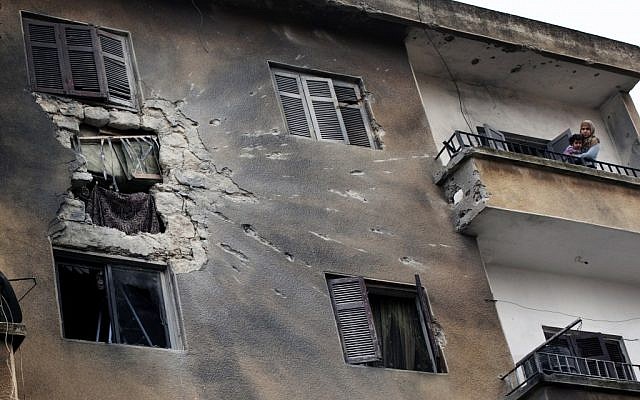A woman holds her daughter on the balcony of a building damaged by Syrian Army sheliing in central Idlib on Monday (photo credit: AP/Rodrigo Abd)
