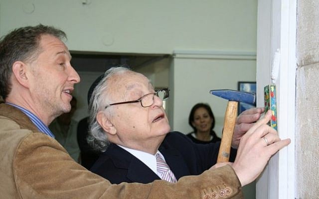 Ambassador Yehuda Avner affixes a mezuza to the front door of The Times of Israel offices in Jerusalem, February 2012. (photo credit: Amanda Borschel-Dan/The Times of Israel)