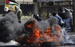 Masked Palestinians throw stones toward Israeli security forces, not pictured, during clashes in the West Bank town of Al-Ram, near Jerusalem, Saturday. (photo credit: AP Photo/Nasser Shiyoukhi)
