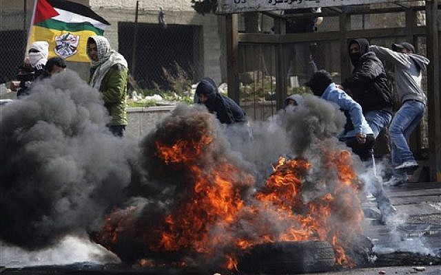 Masked Palestinians throw stones toward Israeli security forces, not pictured, during clashes in the West Bank town of Al-Ram, near Jerusalem, Saturday. (photo credit: AP Photo/Nasser Shiyoukhi) Masked Palestinians throw stones toward Israeli security forces, not pictured, during clashes in the West Bank town of Al-Ram, near Jerusalem, Saturday. (photo credit: AP Photo/Nasser Shiyoukhi)