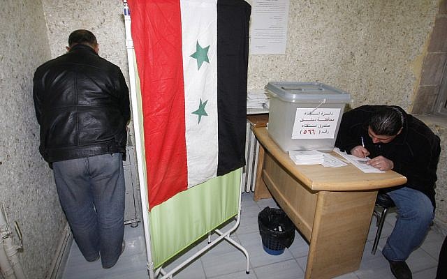A Syrian man, left, signs ballot papers inside a voting booth at a polling station during a referendum on the new constitution in Damascus, Syria, Sunday Feb. 26, 2012 (photo credit: AP/Muzaffar Salman)