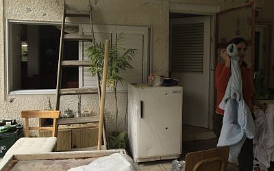 An Israeli woman stand near the entrance to her house in a Gaza border kibbutz, hit by a Kassam rocket earlier this week. (photo credit: Tsafrir Abayov/Flash90)