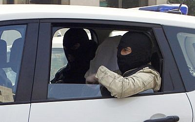 An unidentified man with his head covered, believed to be Abdelkader Merah or his companion, sits between masked police officers as they head to the French police's anti-terrorist headquarters in Levallois-Perret, outside Paris, Saturday, March 24. (photo credit: AP/Christophe Ena)