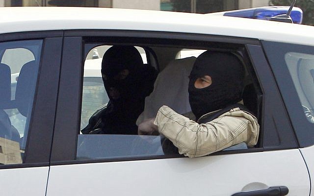 An unidentified man with his head covered, believed to be Abdelkader Merah or his companion, sits between masked police officers as they head to the French police's anti-terrorist headquarters in Levallois-Perret, outside Paris, Saturday, March 24. (photo credit: AP/Christophe Ena)