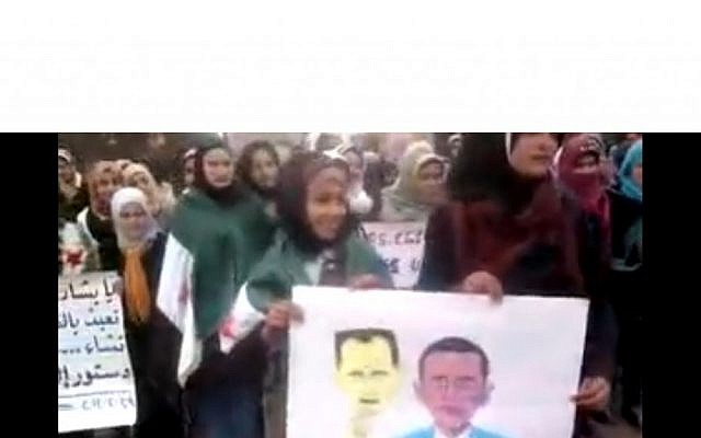 Female student protesters hold a poster of Obama with an Assad mask in Idlib, Syria (photo credit: Shaam News) Female student protesters hold a poster of Obama with an Assad mask in Idlib, Syria (photo credit: Shaam News)