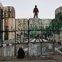 A boy watches an Egyptian female artist and activist at work on the 'No Walls Street' during the graffiti campaign. (photo credit: AP/Nasser Nasser)