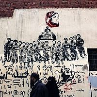 An Egyptian couple walks under a mural depicting female activist Samira Ibrahim, who was forced to undergo a 'virginity test' while in detention by the military. (photo credit: AP/Nasser Nasser)