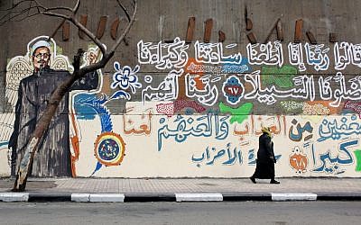 An Egyptian woman walks past a mural with a picture depicting a victim of clashes between protesters and army soldiers in December 2011, with verses of Quran that read in Arabic "God, we obeyed our lords and they misled us, punish them God twice as much and curse them" in Cairo, Egypt. (photo credit: AP Photo/Nasser Nasser)