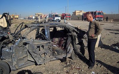 A man stands next to a bombed vehicle in Kirkuk, Iraq (photo credit: AP/Emad Matti)