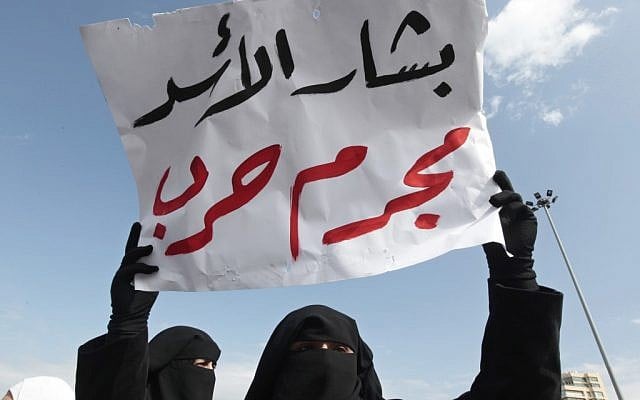 A Lebanese anti-Syrian regime Salafi protester holds a poster in Arabic that reads, "Bashar Assad is a war criminal," at a demonstration in Martyrs' Square, Beirut, March 4. (photo credit: Hussein Malla/AP)