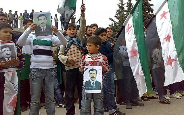 A citizen journalism image of anti-Syrian regime protesters in Idlib, near the Syrian-Turkish border, Friday, holding posters of a man allegedly killed by pro-Syrian forces and raising the Syrian flag. (photo credit: AP/Edlib News Network) A citizen journalism image of anti-Syrian regime protesters in Idlib, near the Syrian-Turkish border, Friday, holding posters of a man allegedly killed by pro-Syrian forces and raising the Syrian flag. (photo credit: AP/Edlib News Network)