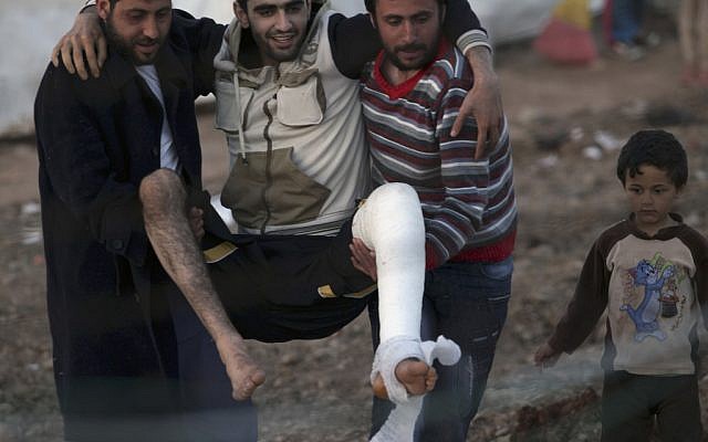 Friends carry an injured Syrian refugee inside their camp in Reyhanli, Turkey (photo credit: Burhan Ozbilici/AP)