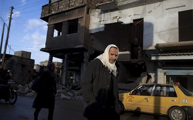 A man walks next to a damaged building due to clashes between the Free Syrian Army and government forces on the outskirts of Idlib, north Syria, Thursday. (photo credit: AP/Rodrigo Abd)