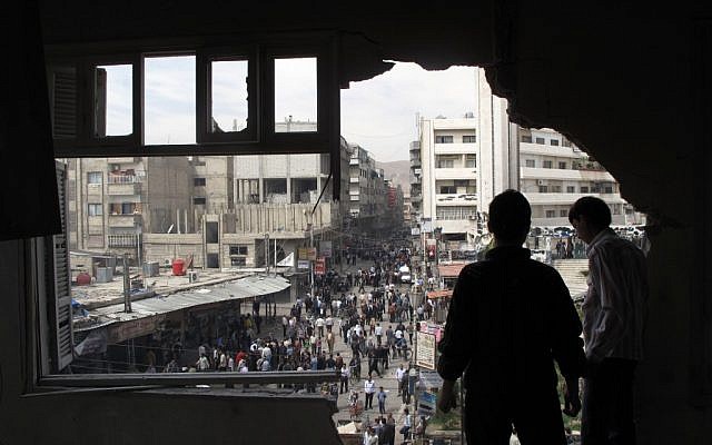 Syrian youth stand in a building damaged by tank shells in Damascus after a raid by Syrian troops killed several rebels and civilians last week (photo credit: AP)