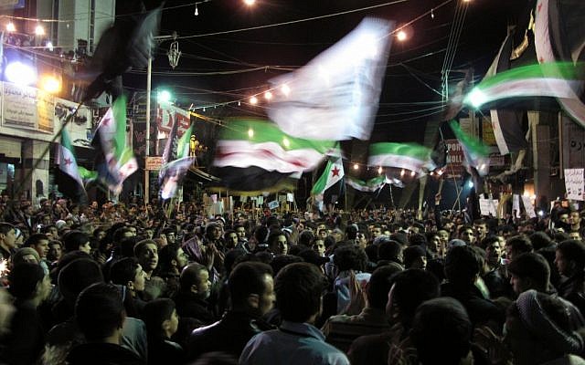 Syrians wave revolutionary flags and chant slogans at a night protest against President Bashar Assad in Damascus neighborhood, Monday (photo credit: AP) Syrians wave revolutionary flags and chant slogans at a night protest against President Bashar Assad in Damascus neighborhood, Monday (photo credit: AP)