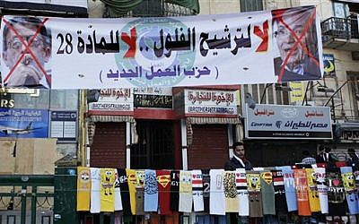 An Egyptian street vendor with t-shirt display at a rally at Tahrir square in Cairo on Friday. The banner reads "No for the former regime candidates, no for article 28, the New Labor Party," and has pictures of two presidential hopefuls crossed out. (photo credit: AP Photo/Nasser Nasser)