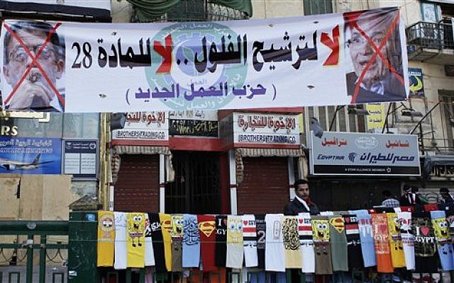 An Egyptian street vendor with t-shirt display at a rally at Tahrir square in Cairo on Friday. The banner reads "No for the former regime candidates, no for article 28, the New Labor Party," and has pictures of two presidential hopefuls crossed out. (photo credit: AP Photo/Nasser Nasser)