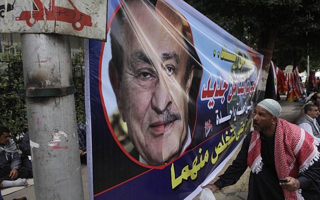 An Egyptian holds a banner showing a half face portrait of ousted president Hosni Mubarak, left, and his former spy chief Omar Suleiman during a rally in Tahrir Square, Cairo, Friday. The Arabic text reads "We will protect our revolution". (photo credit: AP/Amr Nabil)