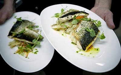 Israeli chef Noam Dekkers of Liliyot restaurant holds two versions of a fish dish, one kosher for Passover and another served on a piece of bread, right, at a restaurant in Tel Aviv. (photo credit: AP)