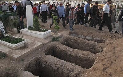 Mourners walk past open graves at a cemetery during a funeral for four people killed in a raid by government forces in a neighborhood of Damascus, Syria, April 7, 2012 (photo credit: AP)