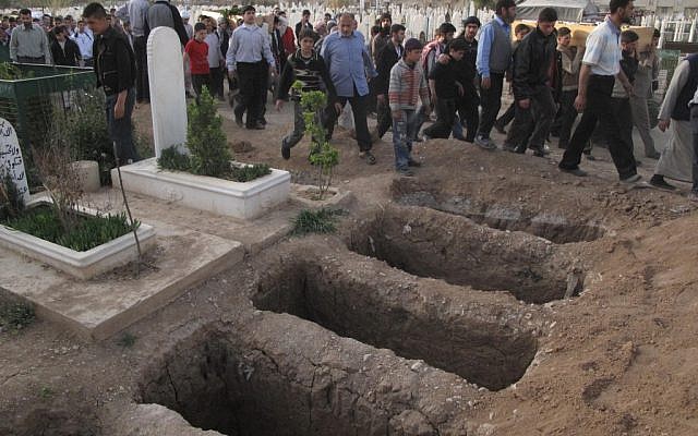Mourners walk past open graves at a cemetery during a funeral for four people killed in a raid by government forces in a neighborhood of Damascus, Syria, April 7, 2012 (photo credit: AP)