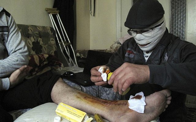 An injured man gets treated in a Damascus neighborhood Tuesday (photo credit: AP)