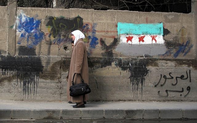 A Syrian woman walks past a painting of the Syrian flag and a sign that reads "Only al-Arour," the name of an Islamic cleric living in Saudi Arabia who opposes President Bashar Assad, in Damascus Monday (photo credit: AP)