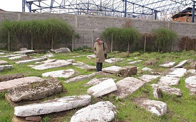 Ruben Fuks, president of the Federation of Serbian Jewish Communities, in the Nis Cemetery, with the new construction in the background. (photo credit: Ruth Ellen Gruber/JTA)