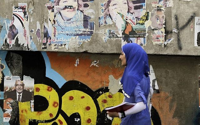 An Egyptian woman passes by a wall with defaced posters of presidential candidates in Cairo, Egypt on Monday. (photo credit: Hasan Jamali/AP)