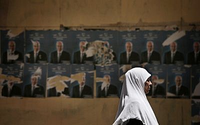 An Egyptian woman walks past defaced posters of Egyptian presidential candidate Ahmed Shafiq in Cairo (photo credit: AP Photo/Manu Brabo)
